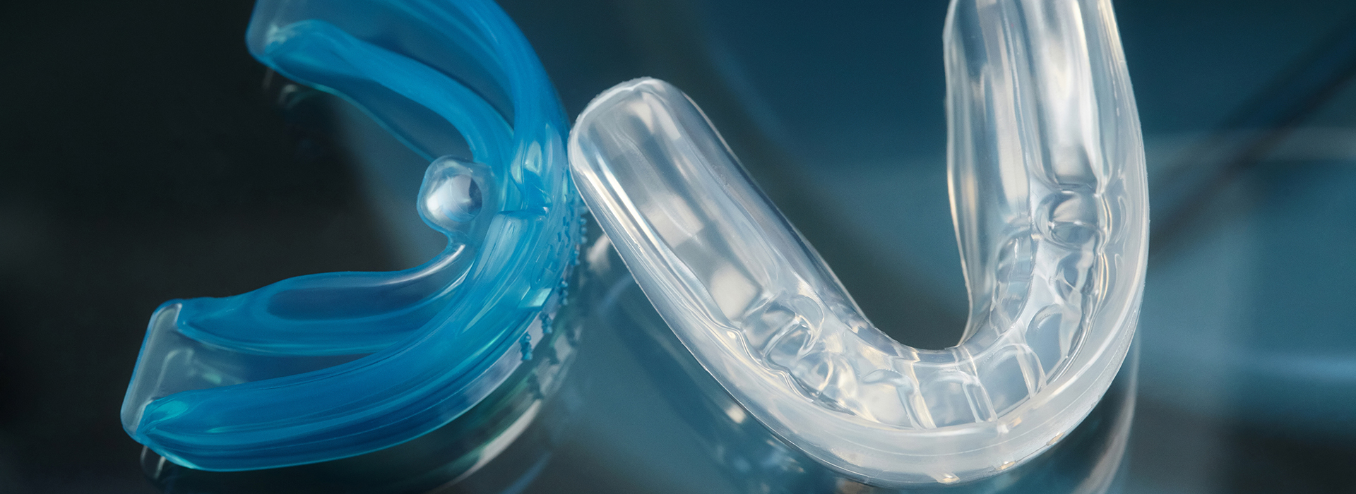 The image shows a clear plastic toothbrush with blue bristles, placed against a dark background.